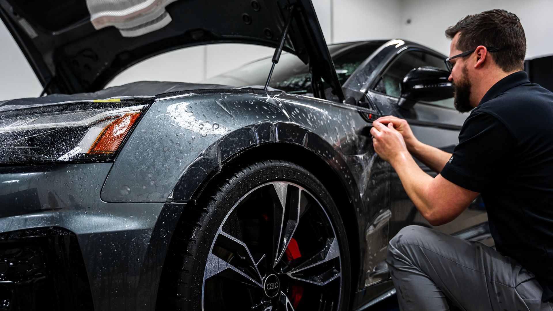 A man is applying a protective film to the side of a car.