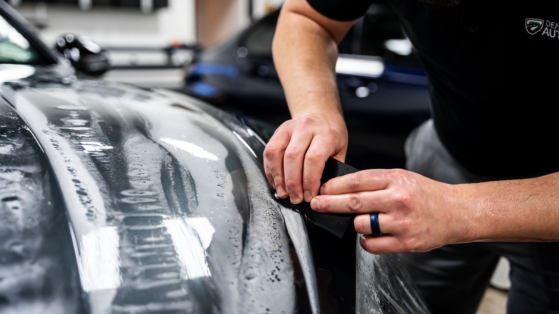 A man is applying a protective film to the hood of a car.