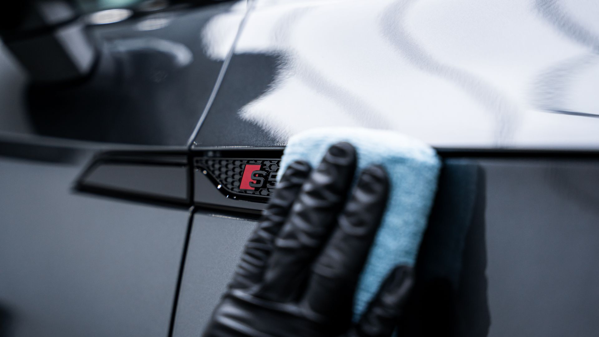 A person is cleaning a car with a sponge and gloves.