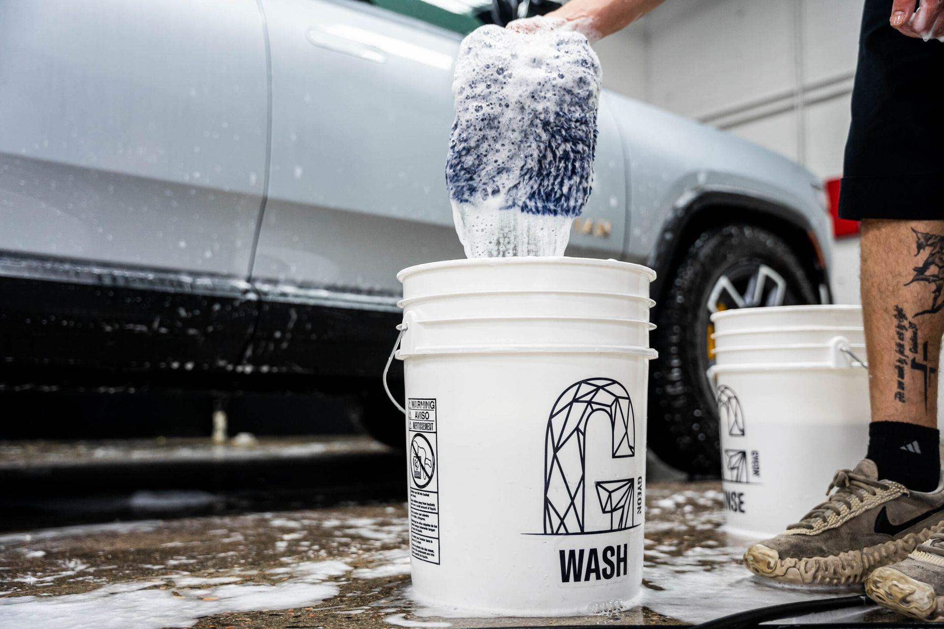 A person is pouring soap into a bucket next to a car.