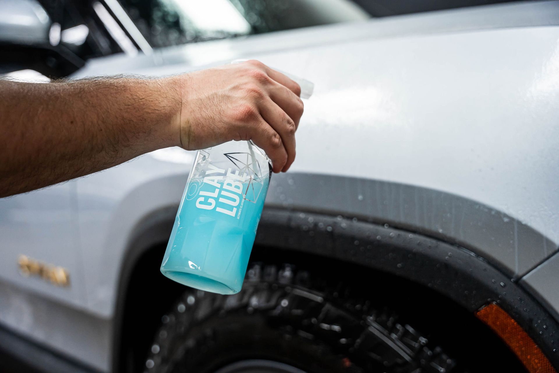 A person is spraying a bottle of clay lube on a car.