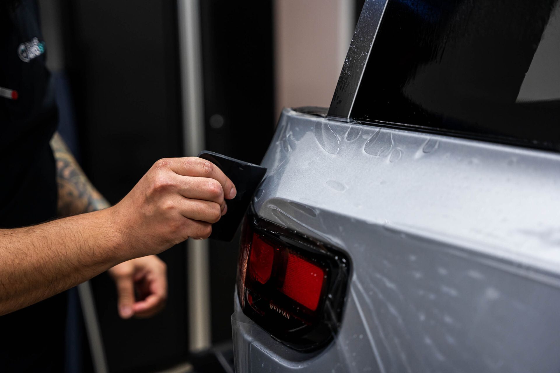 A person is applying a protective film to the back of a car.