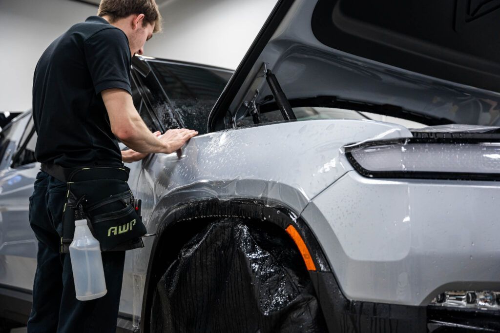 A man is applying a protective film to the side of a car.