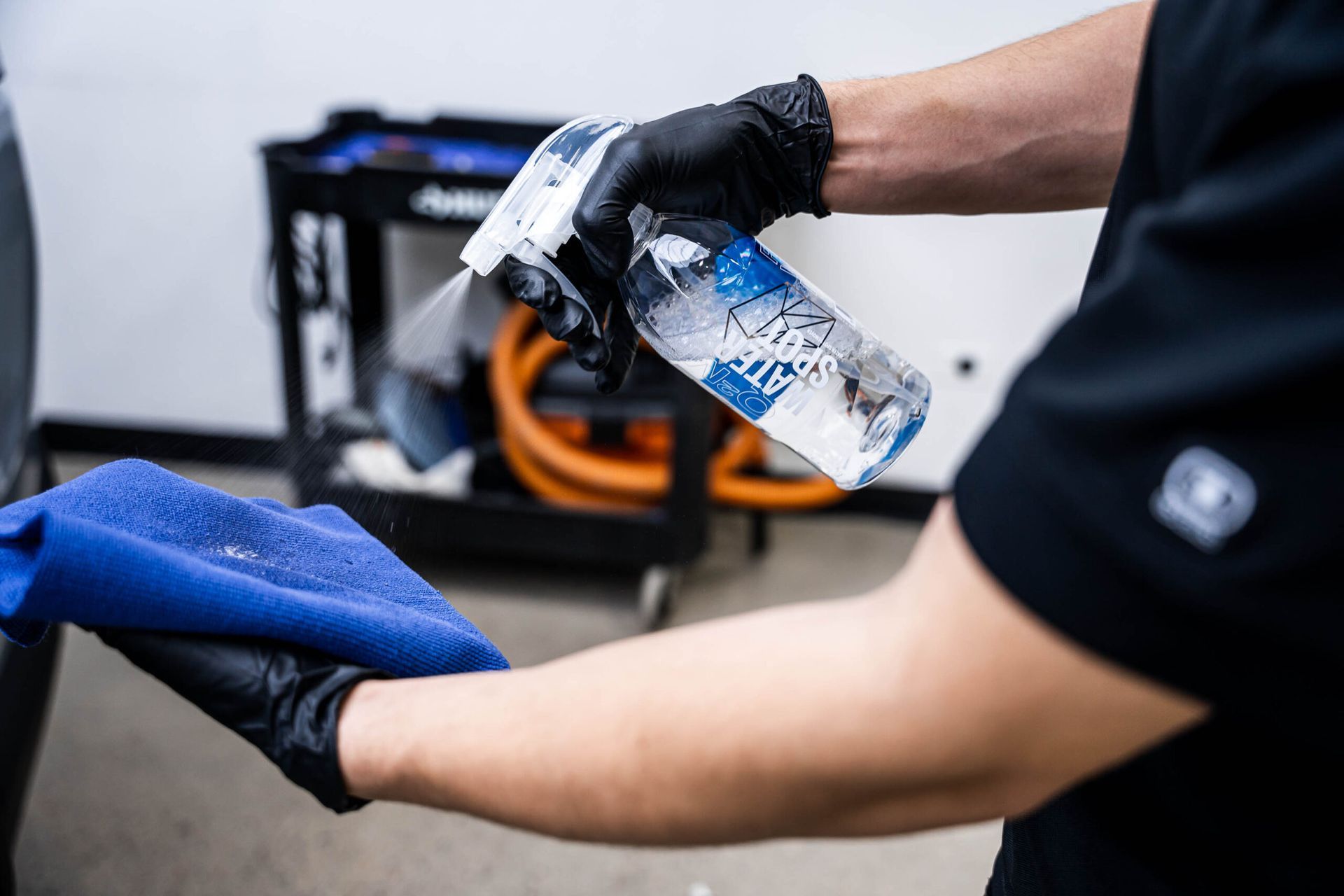 A man wearing black gloves is holding a spray bottle and a blue towel.