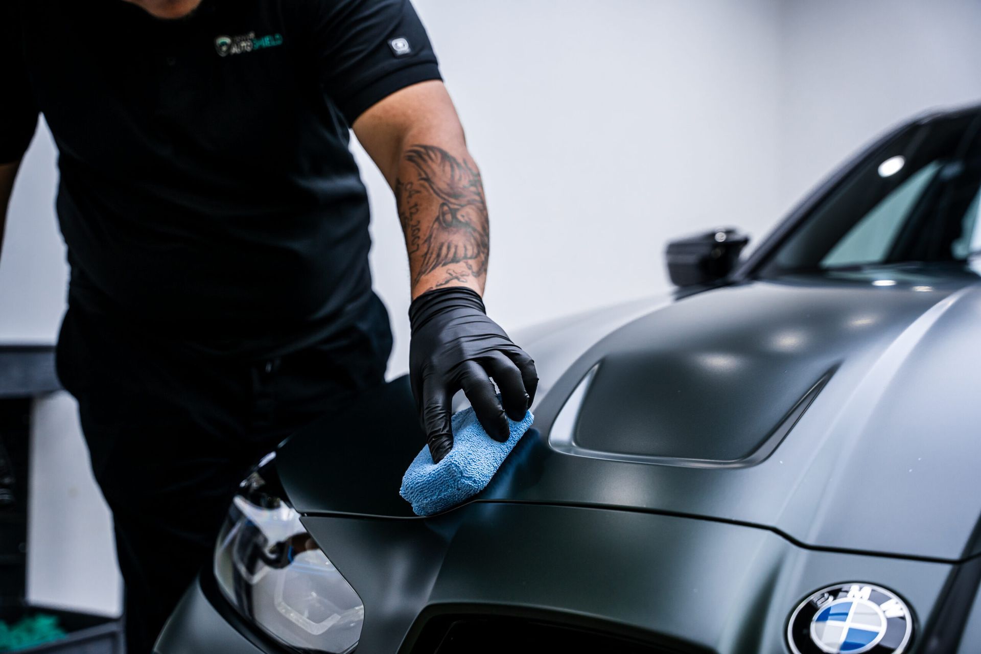 A man is cleaning the hood of a bmw with a sponge.