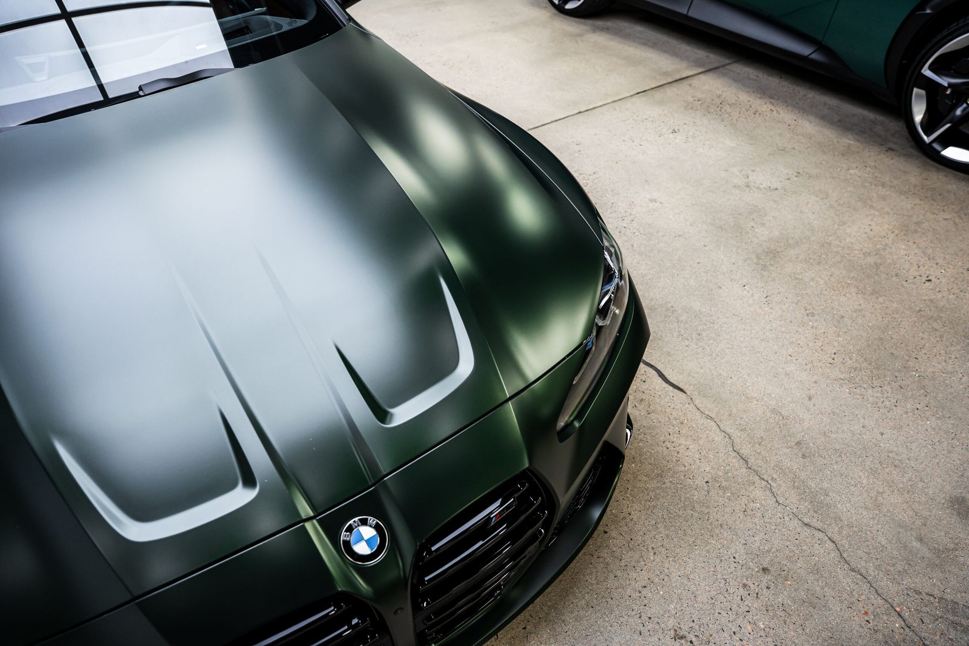 A green bmw is parked in a garage next to another green car.