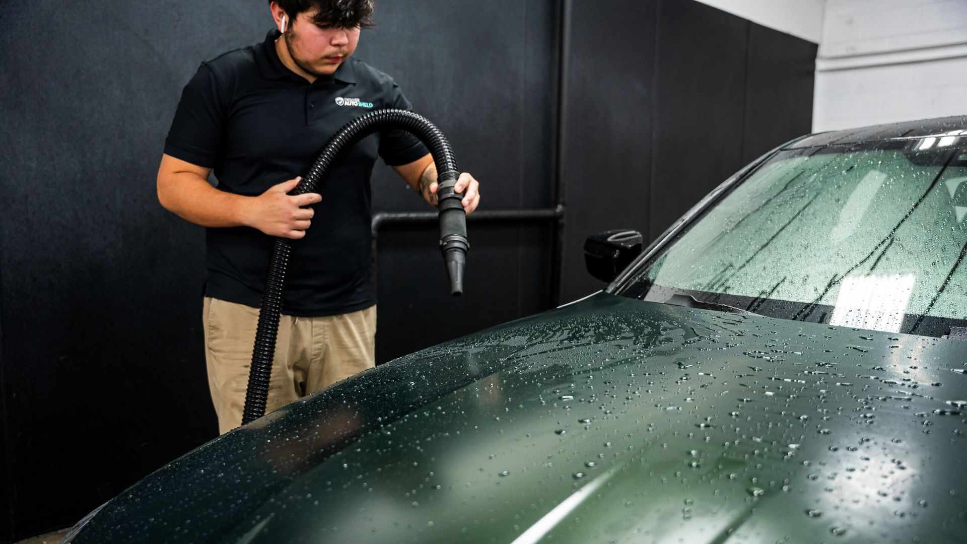 A man is cleaning the hood of a car with a hose.