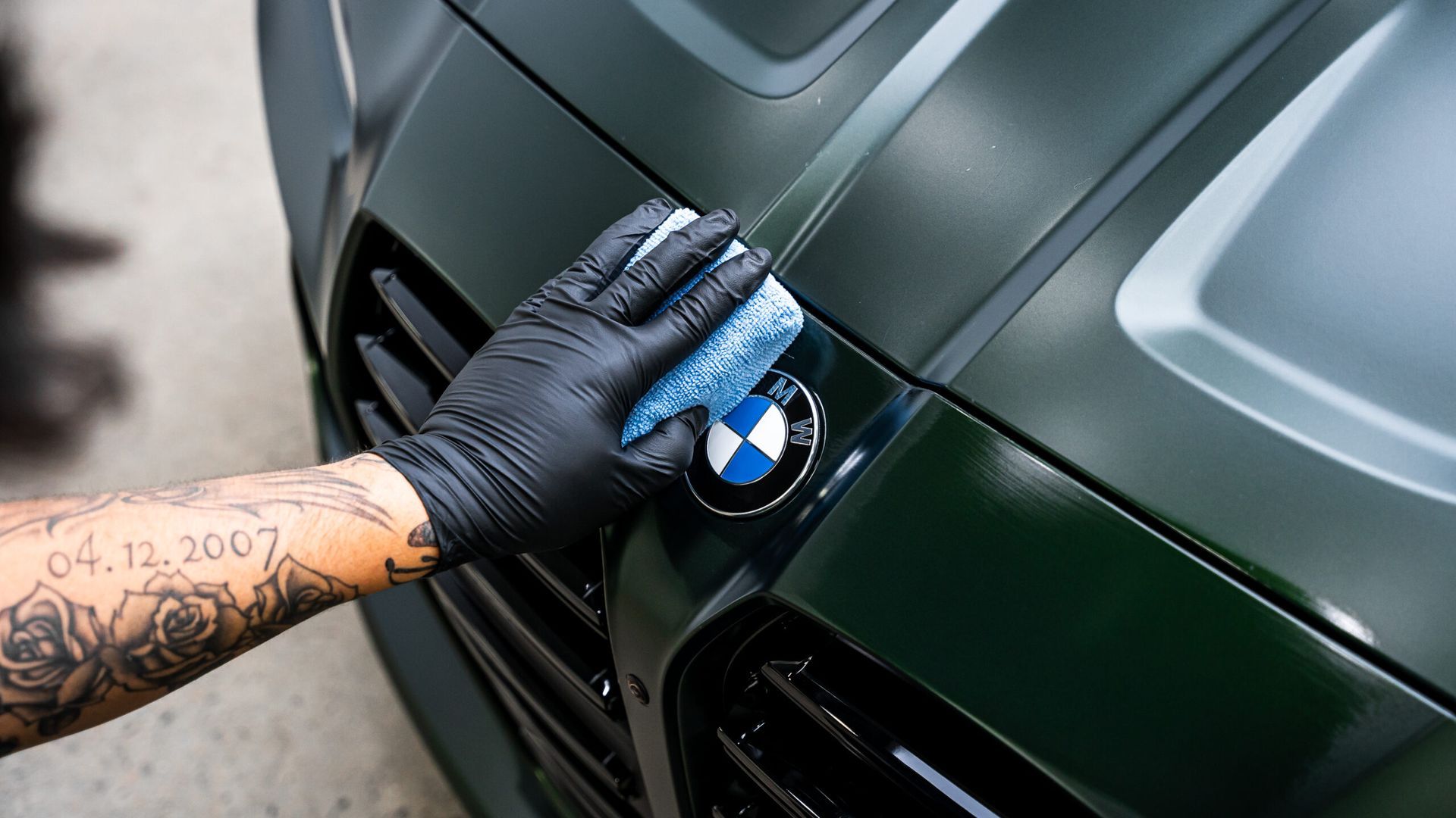 A person with a tattoo on their arm is cleaning the bmw emblem on a car.