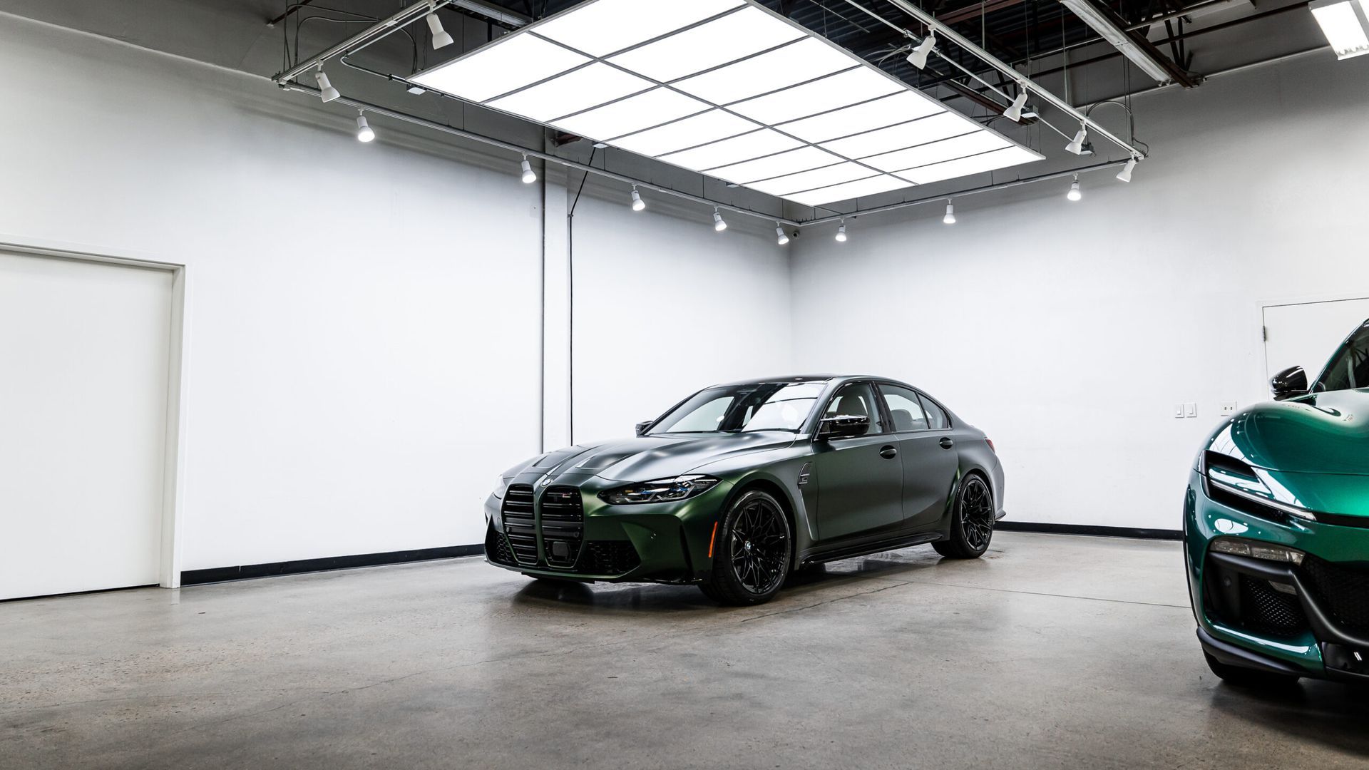 A green bmw m3 is parked in a garage next to another green car.