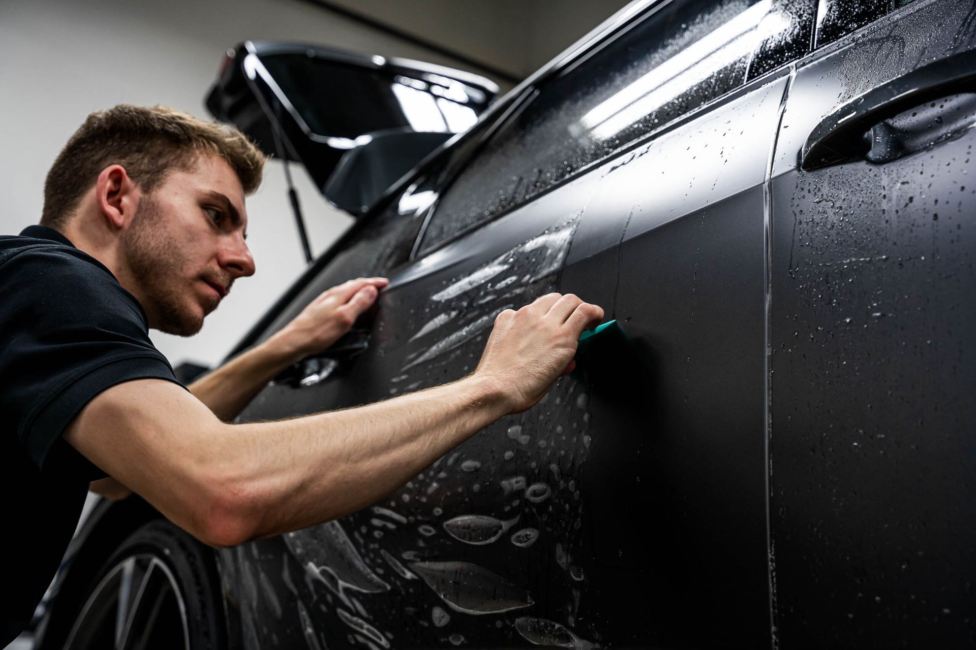 A man is applying a film to the side of a black car.