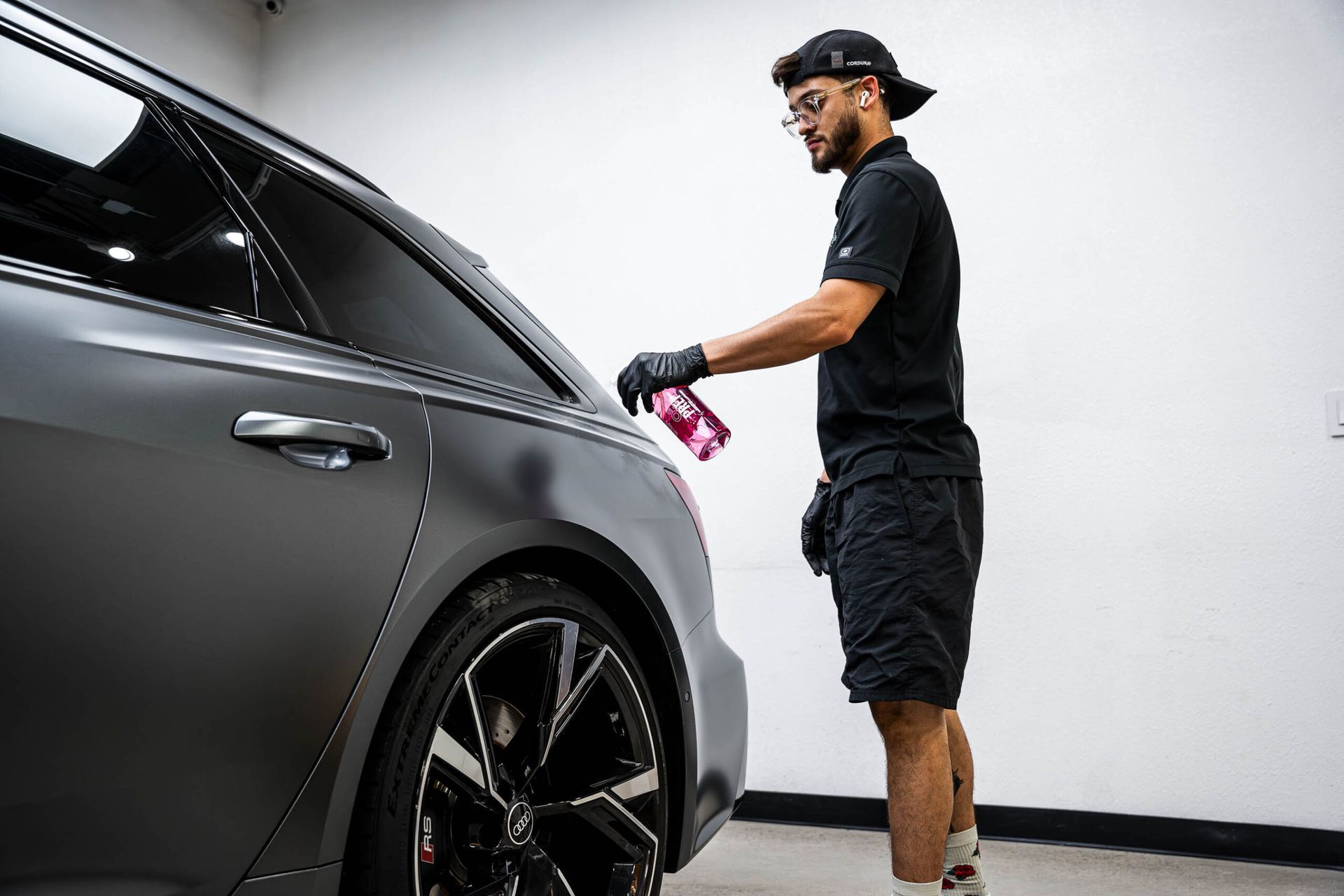 A man is spraying a car with a spray bottle in a garage.