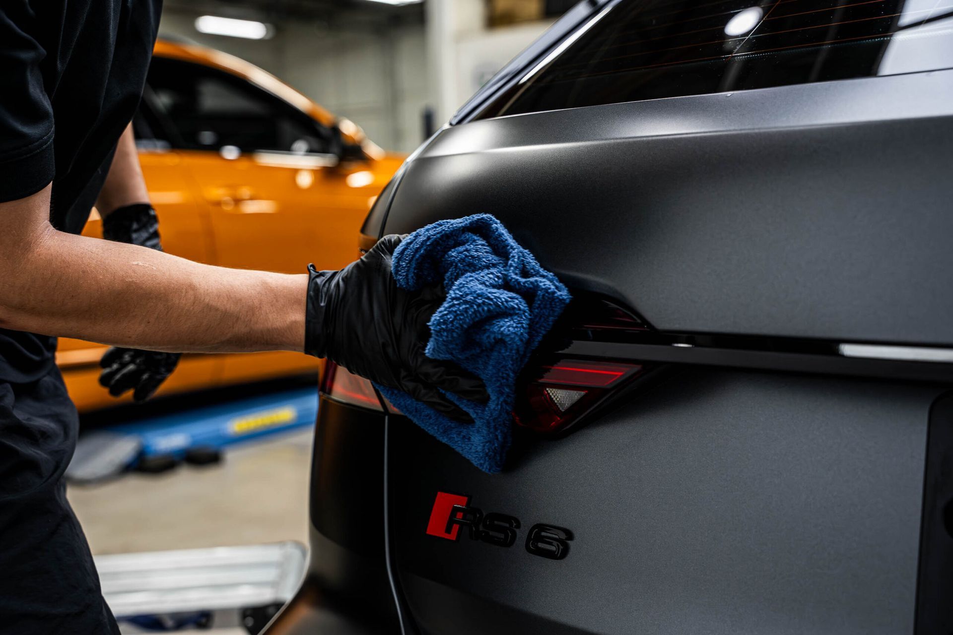 A man is cleaning the back of a car with a blue cloth.