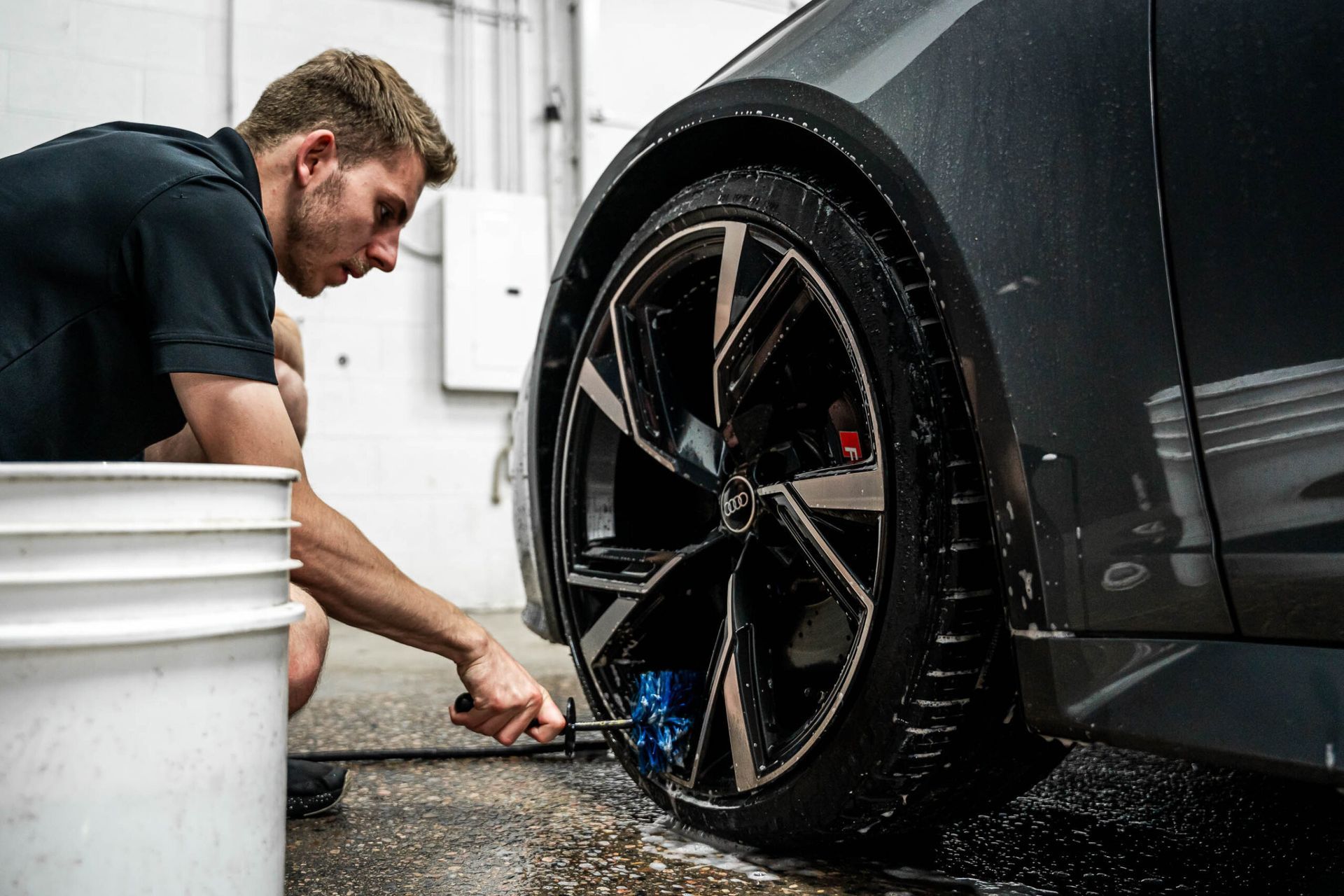 A man is cleaning a car wheel with a brush.