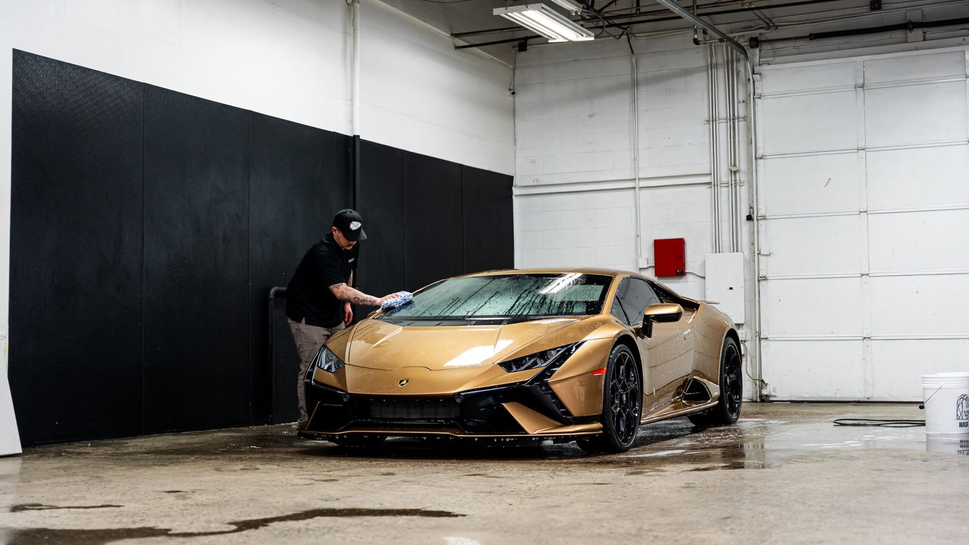 A man is washing a gold lamborghini huracan in a garage.