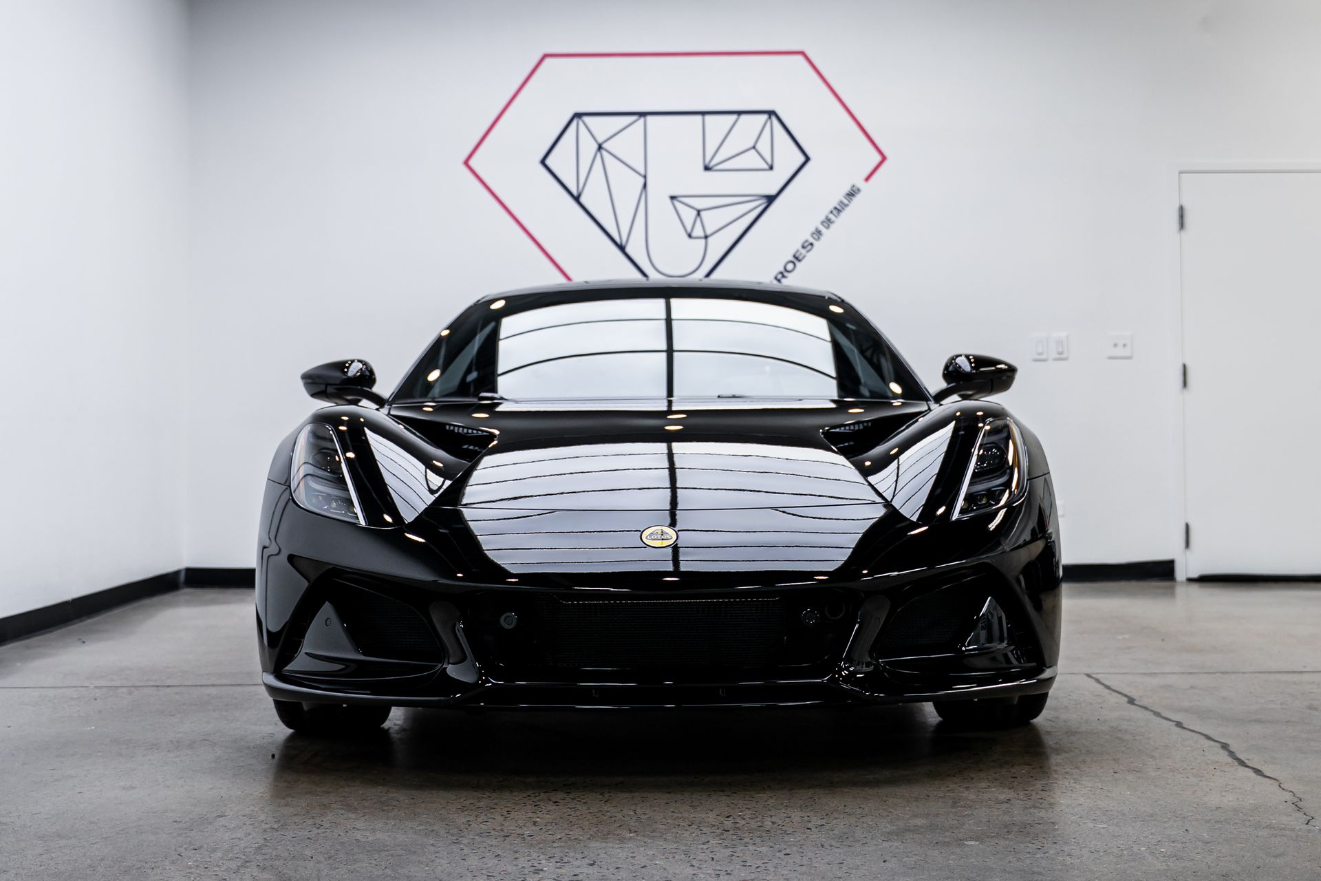 A black sports car is parked in a garage with a diamond on the wall behind it.
