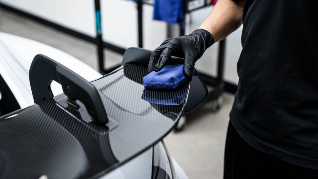 A person is cleaning the spoiler of a car with a cloth.