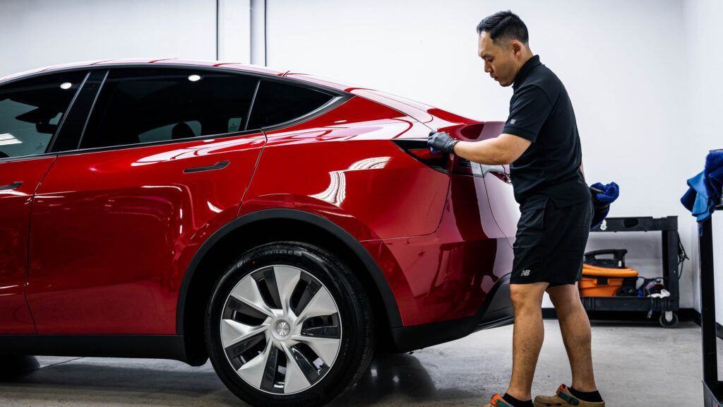 A man is standing next to a red car in a garage.