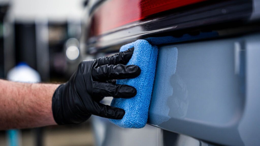 A person is cleaning a car with a blue sponge.