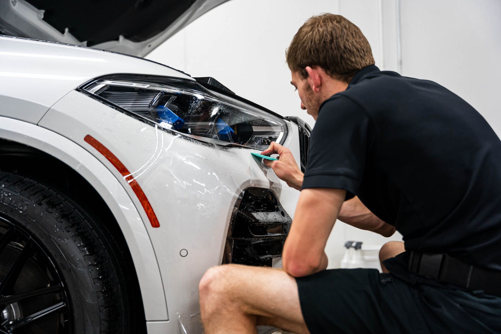 A man is kneeling down next to a white car.