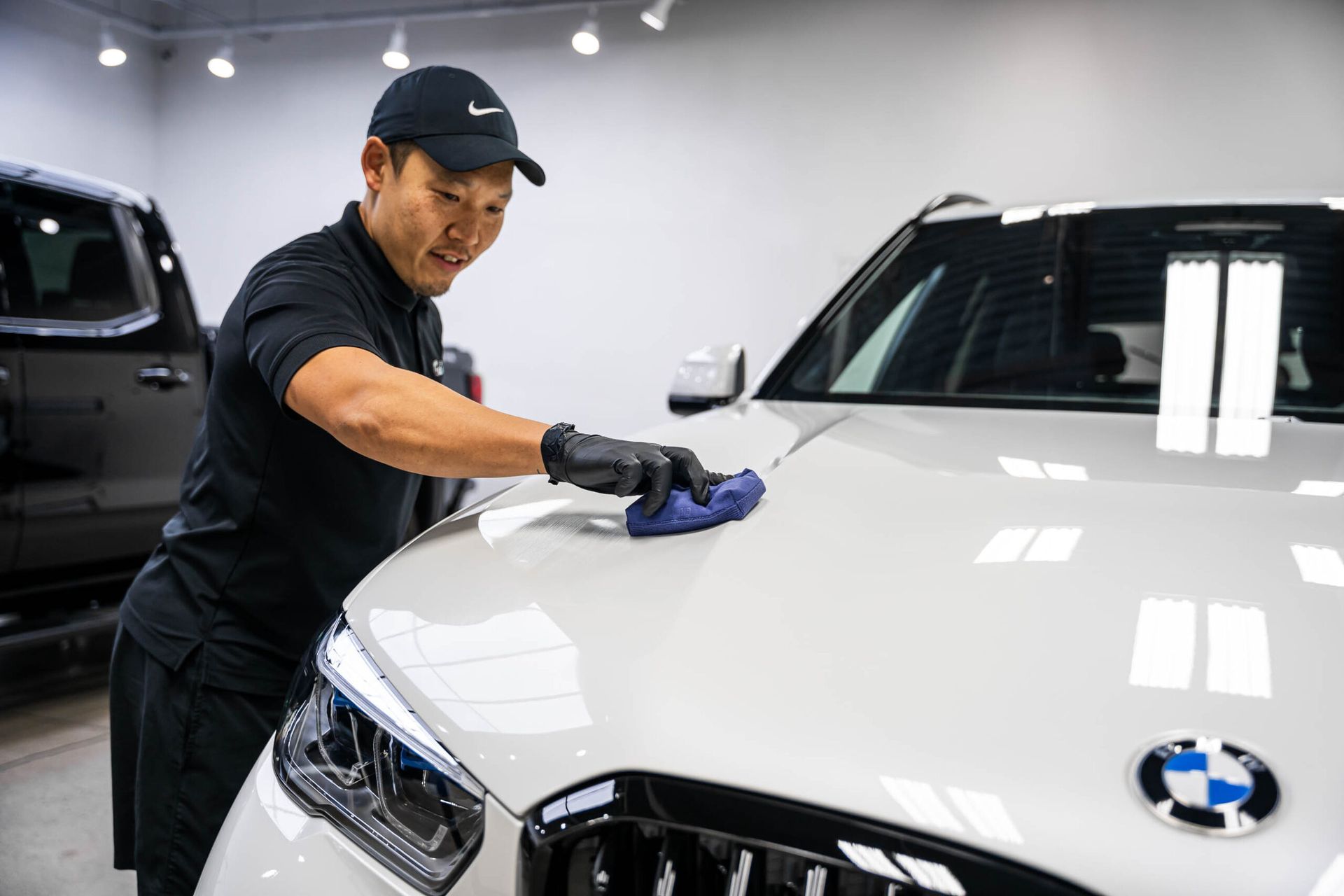 A man is cleaning the hood of a white bmw in a garage.