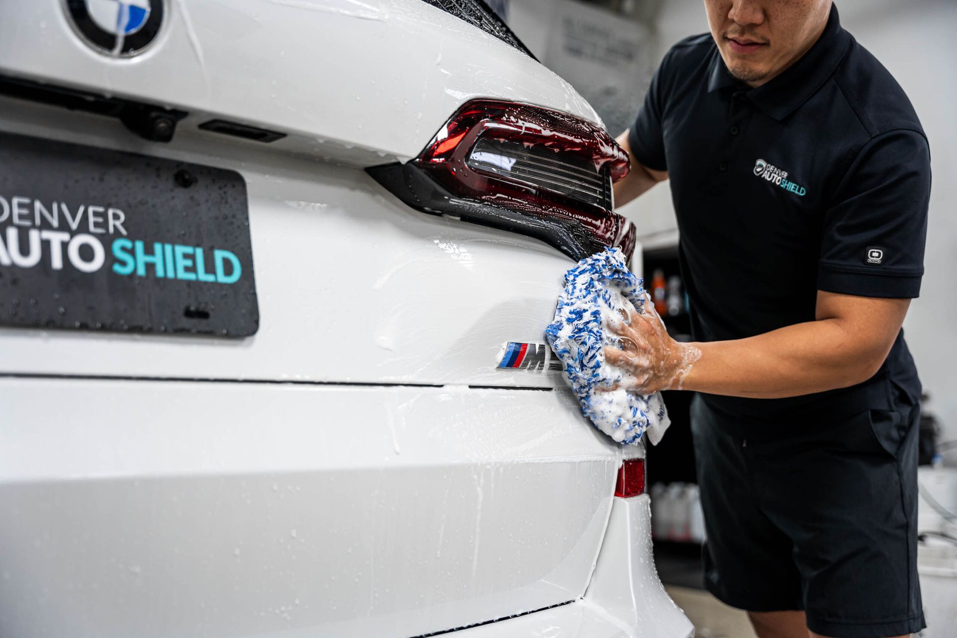 A man is cleaning the back of a white car with a cloth.