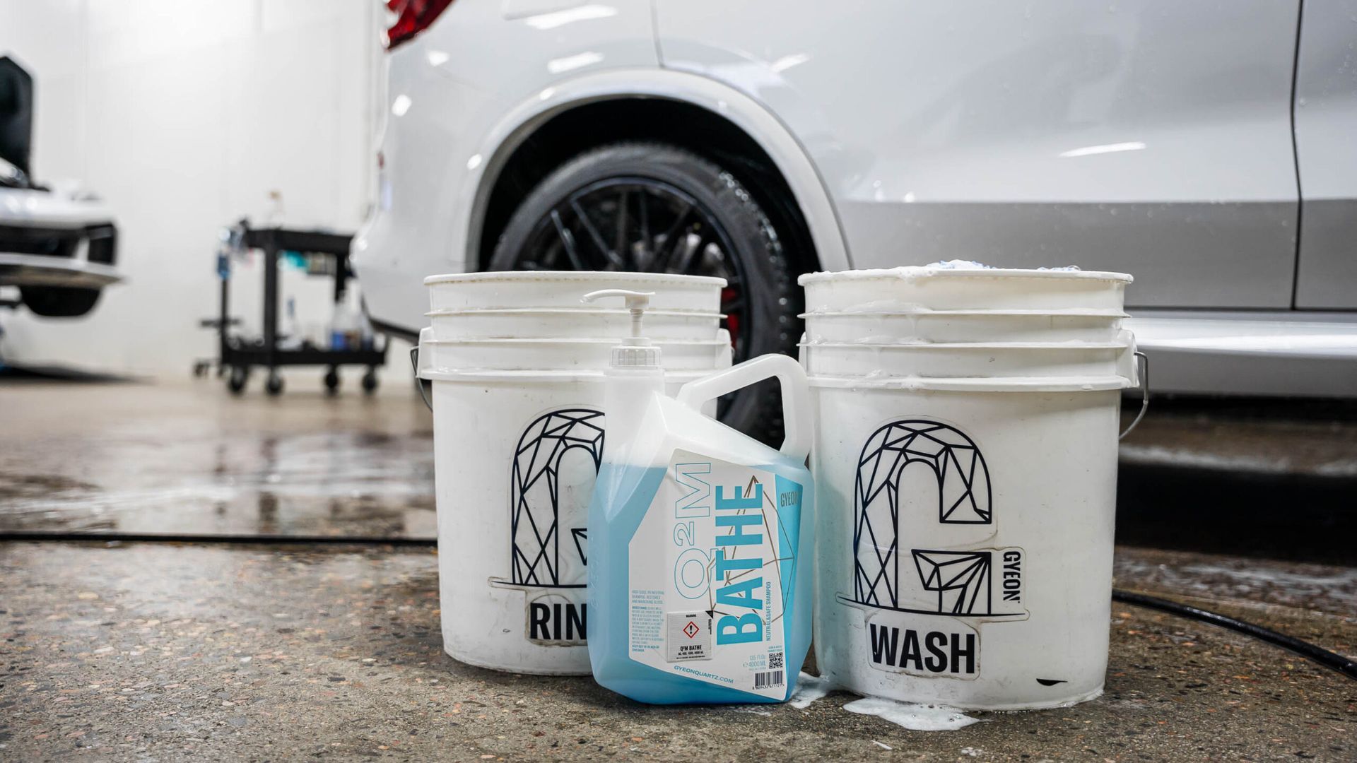 Three buckets of cleaning supplies are sitting next to a car in a car wash.