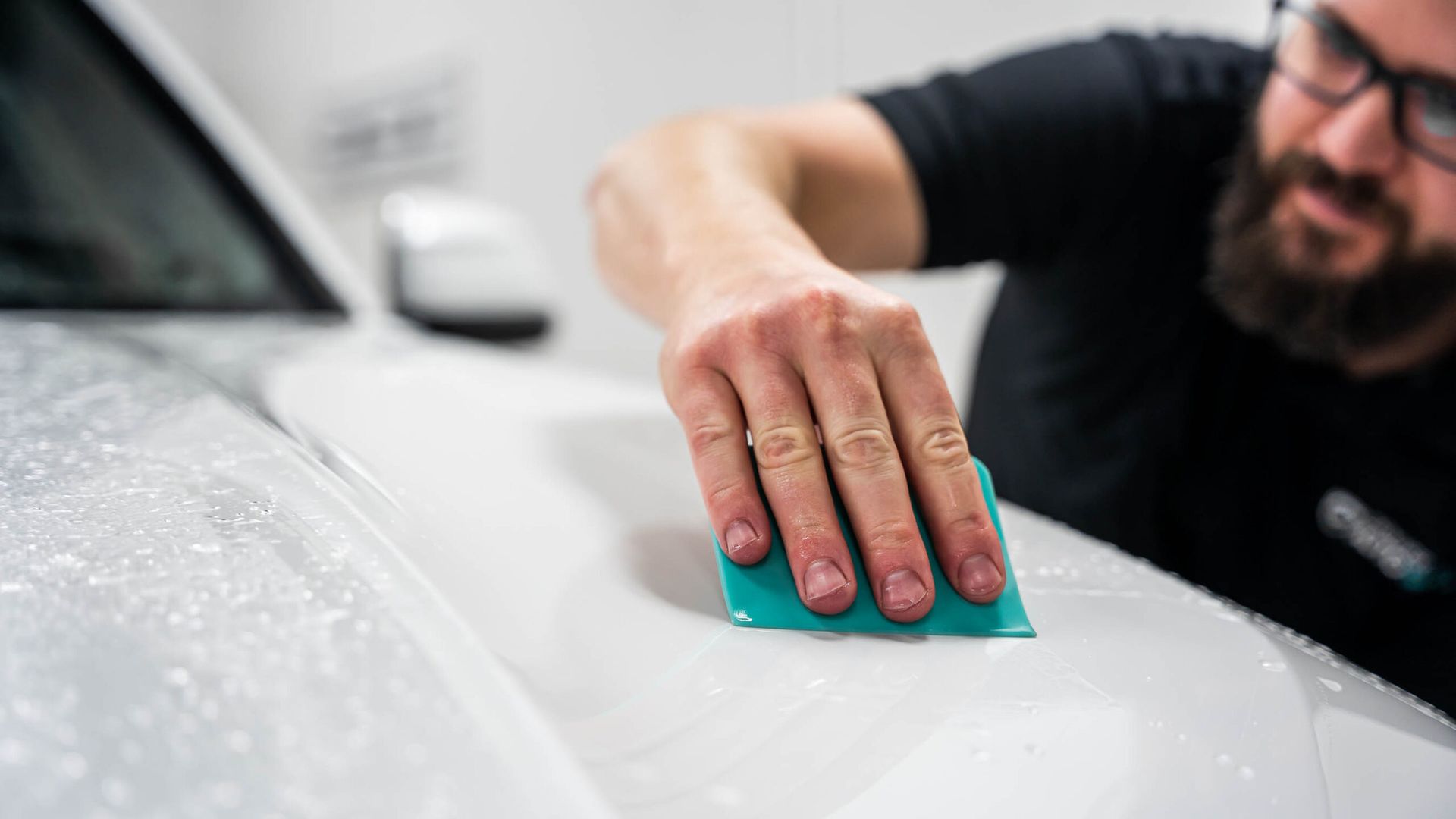 A man is cleaning a white car with a green cloth.