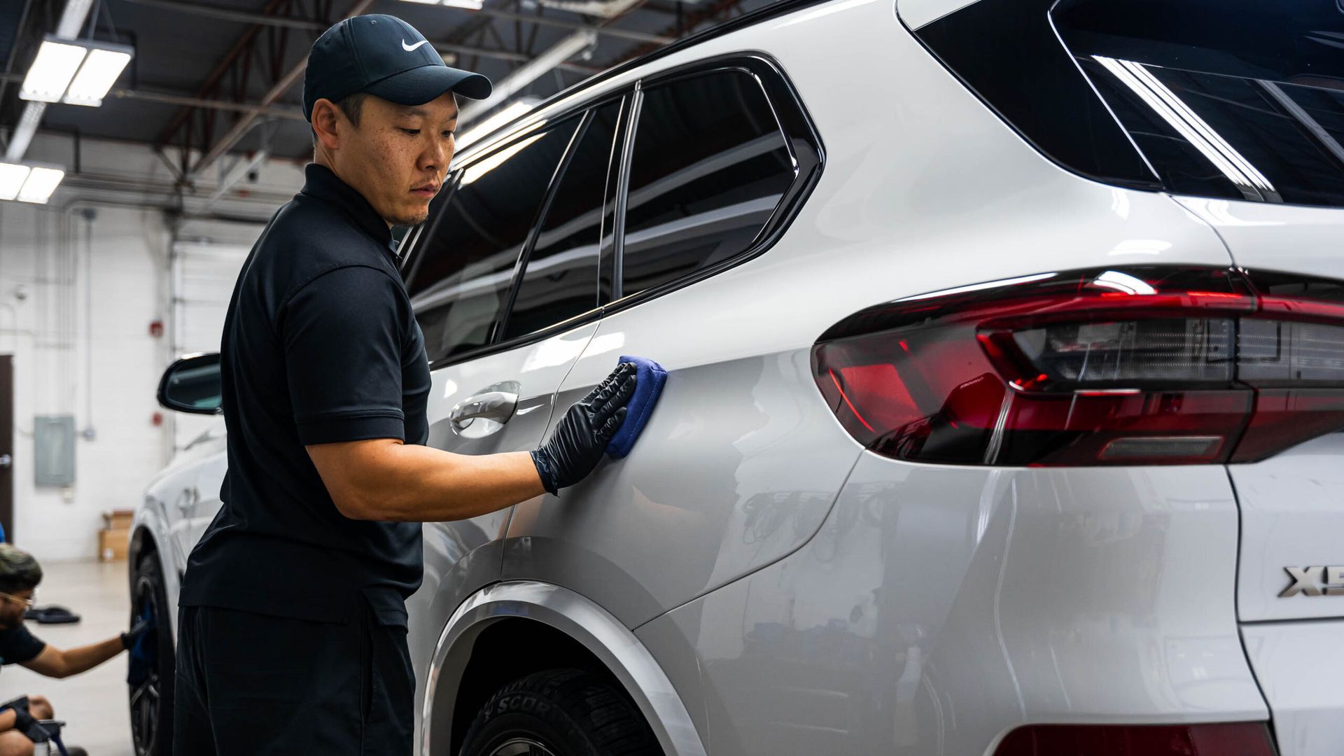 A man is cleaning the side of a silver car in a garage.