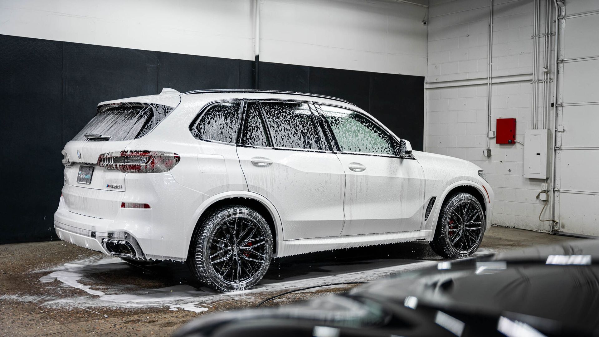 A white bmw x5 is covered in foam in a garage.