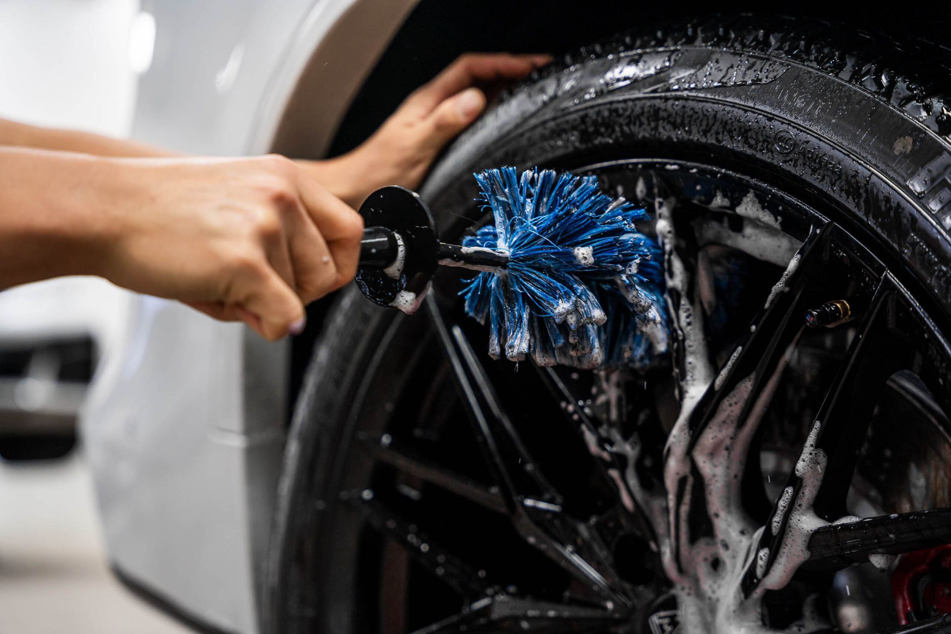 A person is cleaning a car wheel with a brush.