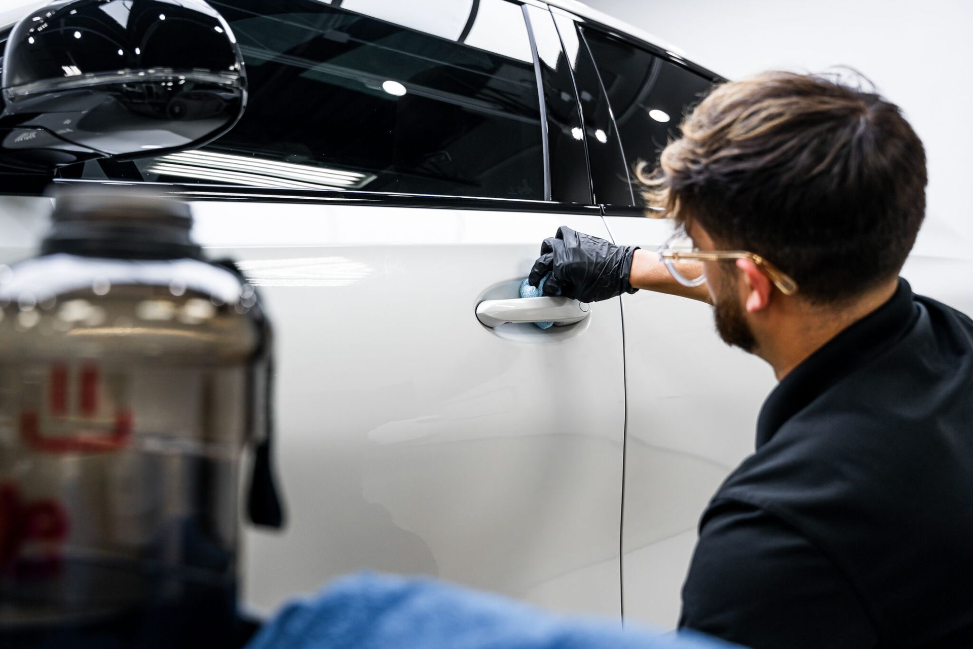 A man is polishing the door handle of a white car.