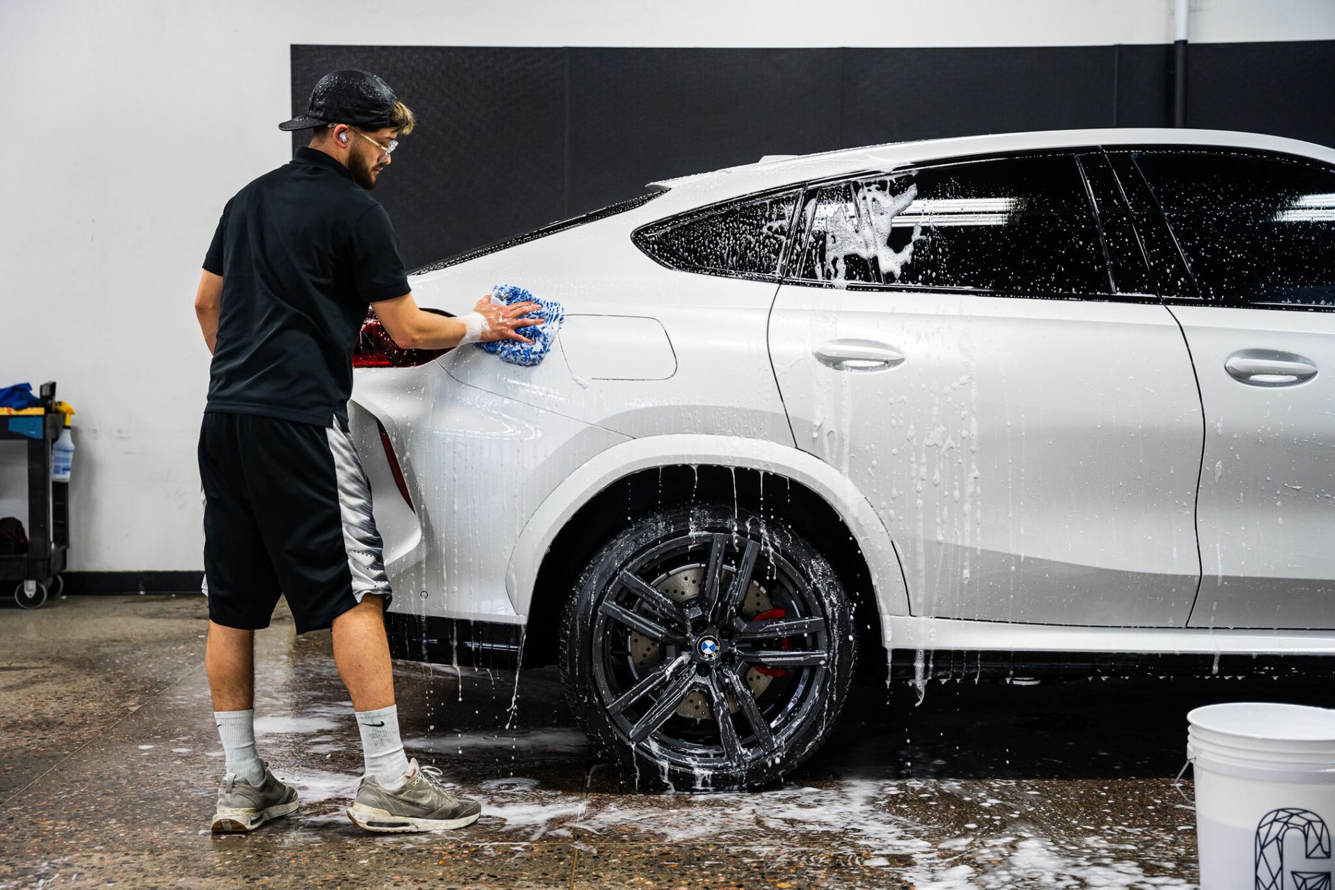 A man is washing a white car in a garage.