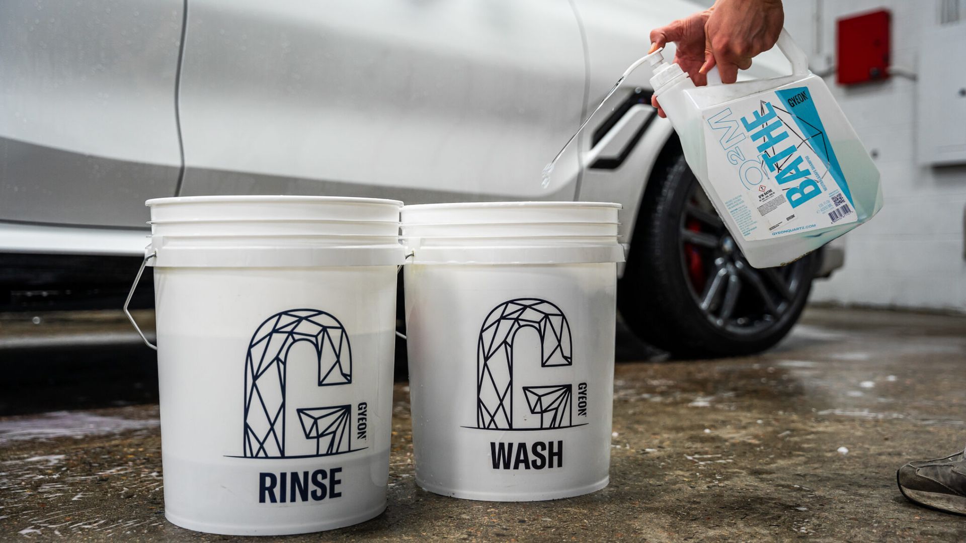 A person is pouring water into two buckets next to a car.