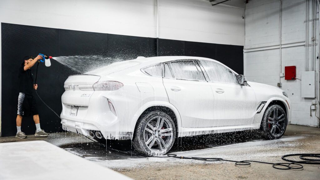 A man is washing a white car with foam in a garage.