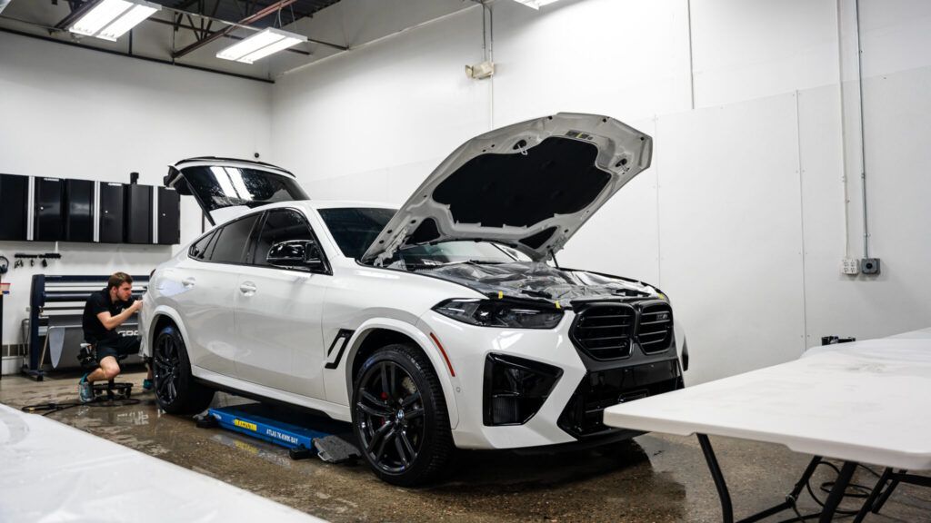 A man is working on a white car in a garage with the hood open.