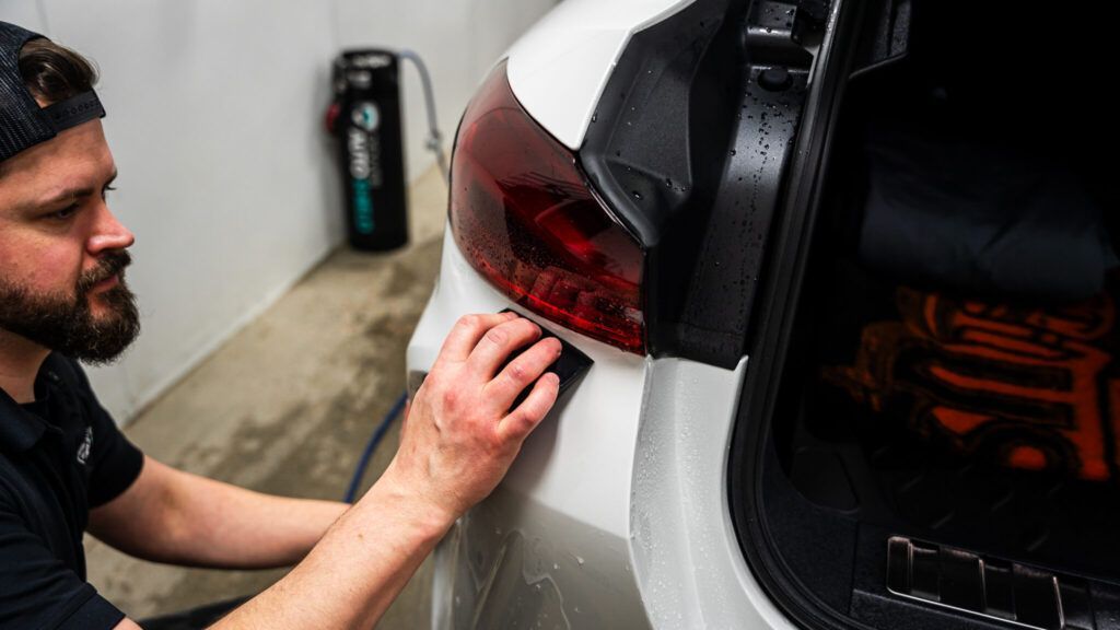 A man is wrapping the tail light of a white car.