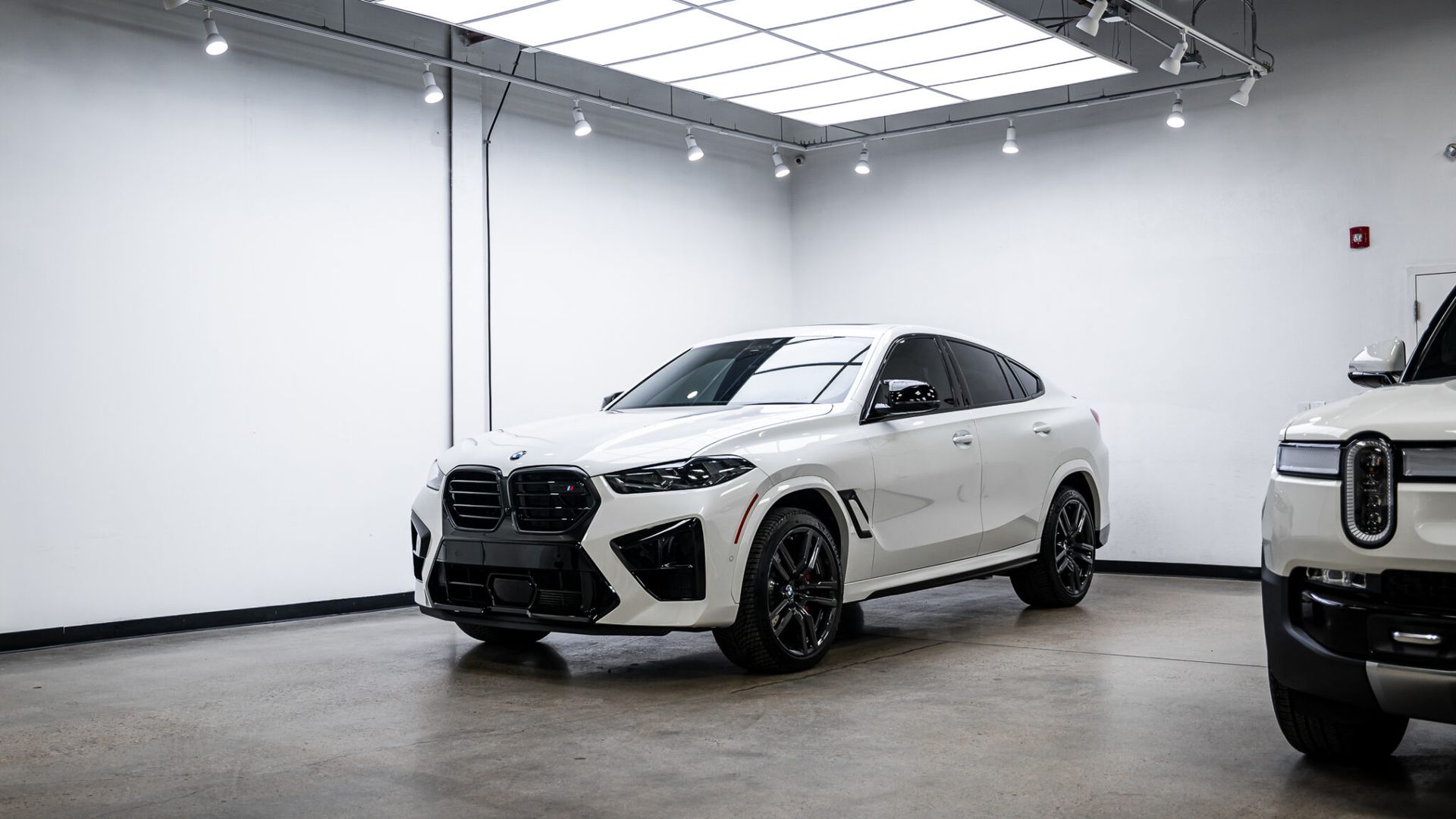 Two white cars are parked in a garage.