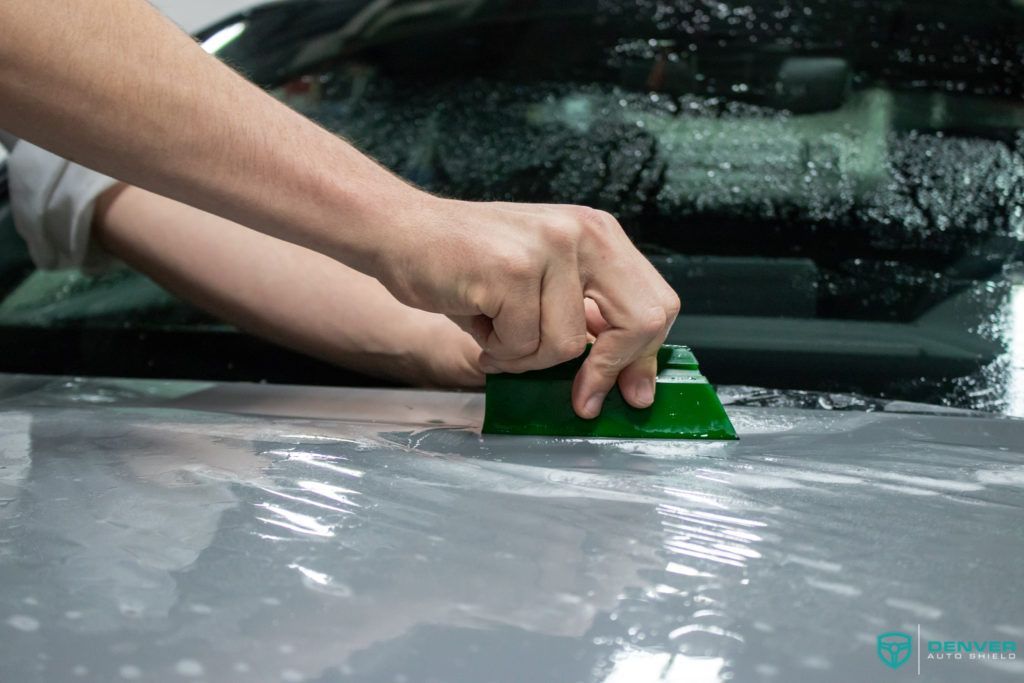 A person is cleaning the windshield of a car with a green sponge.