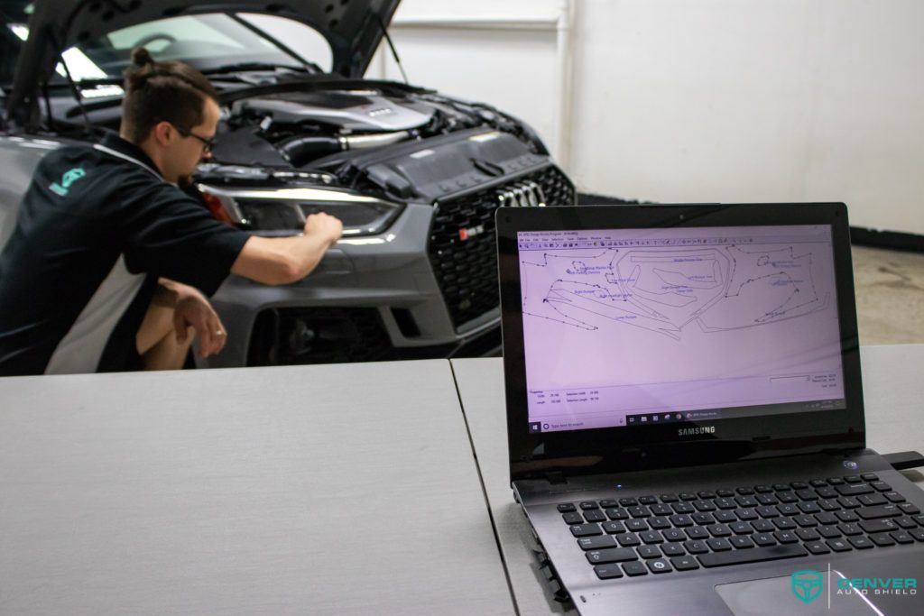 A man is working on the engine of a car next to a laptop.