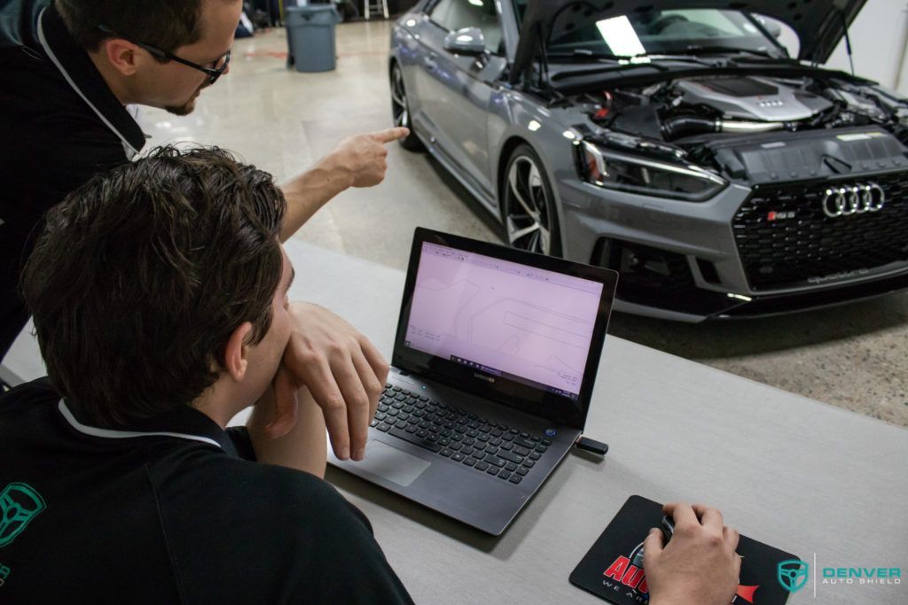 Two men are looking at a laptop in front of a car with the hood open.