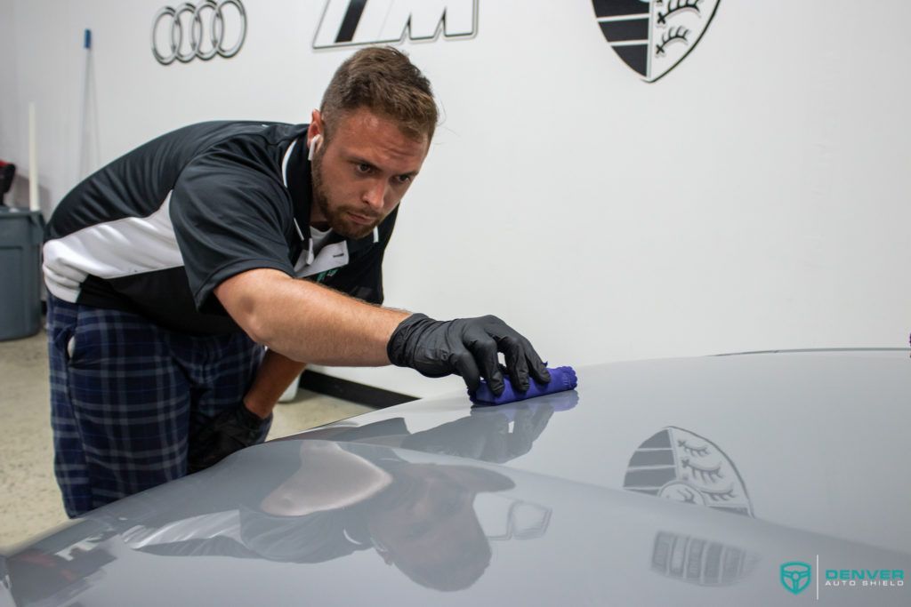 A man is cleaning the hood of a car with a cloth.