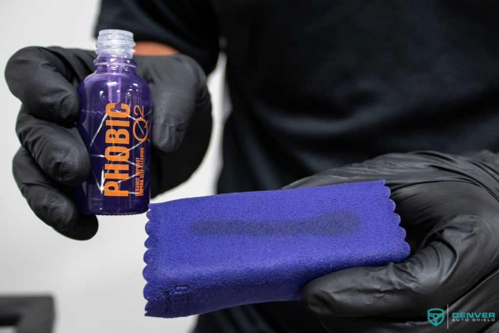 A person wearing black gloves is holding a bottle of phobic oil and a purple cloth.