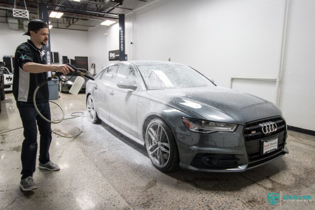 A man is washing a car with a hose in a garage.