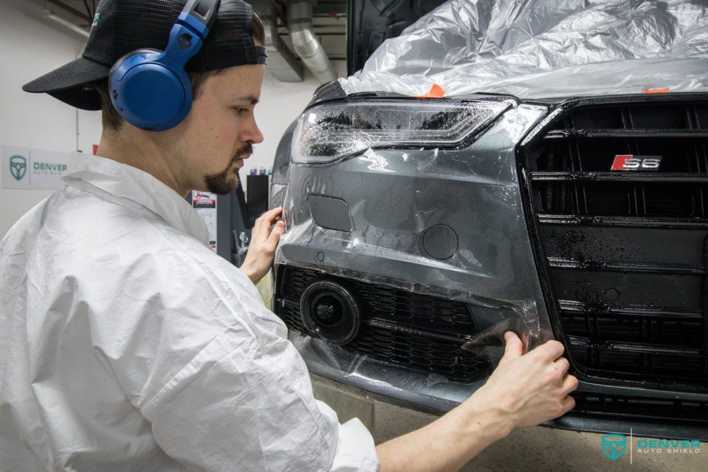 A man wearing headphones is applying a protective film to the front of a car.