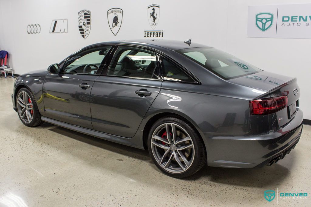 A gray car is parked in a garage in front of a wall with logos on it.