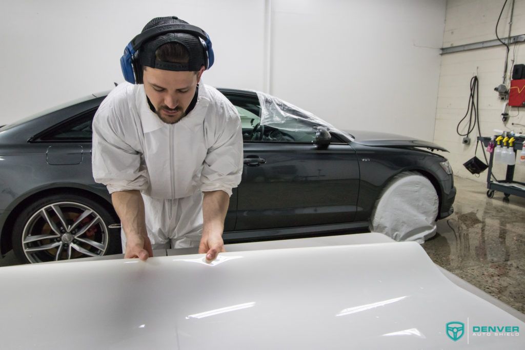 A man is wrapping the hood of a car in a garage.