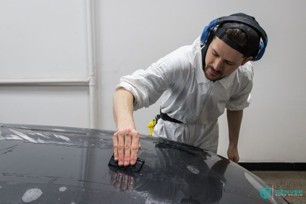 A man wearing headphones is cleaning the hood of a car.