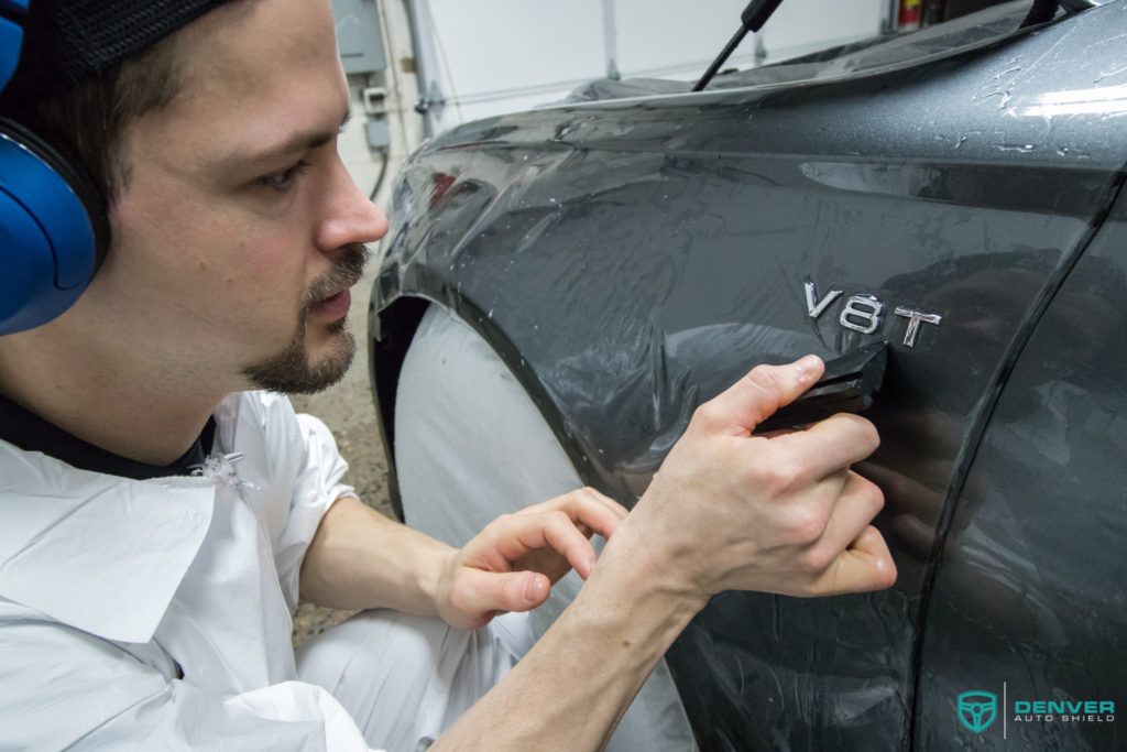 A man wearing headphones is wrapping a car with a protective film.