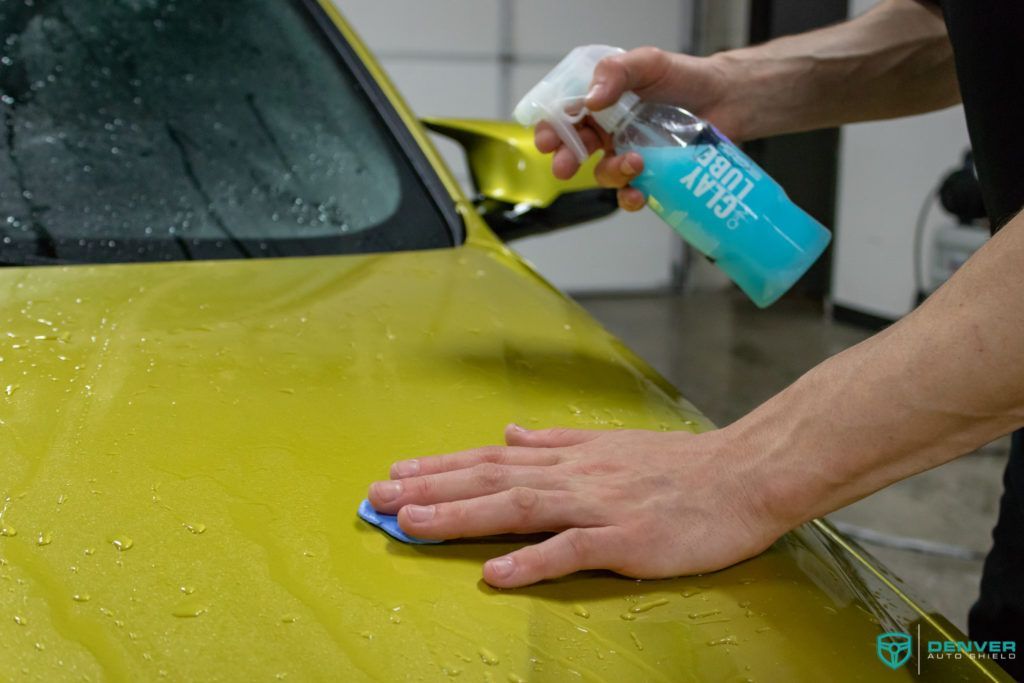 A person is cleaning a yellow car with a cloth and spray bottle.