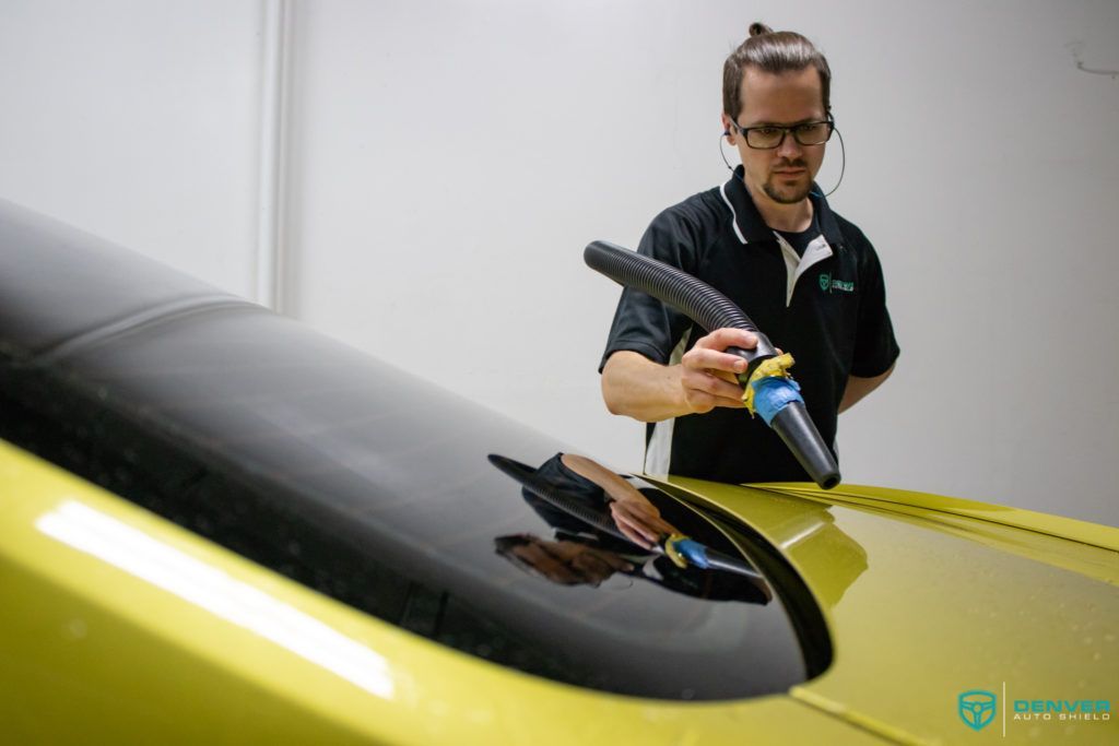 A man is polishing the windshield of a yellow car.